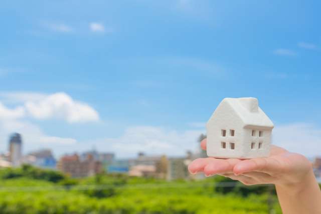 青空と家の模型を持った手