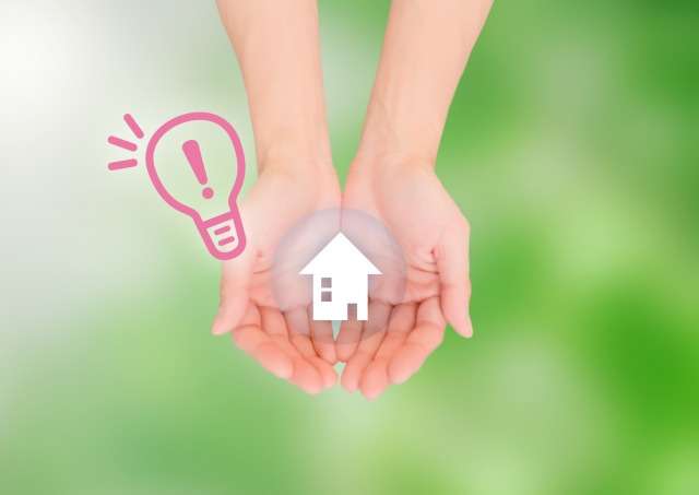 手に包まれた家の切り絵と電球